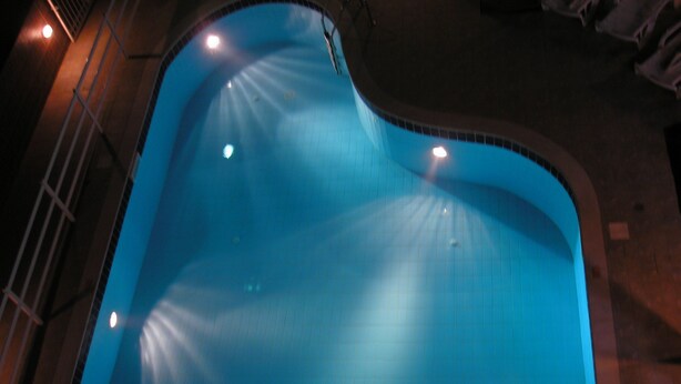 A swimming pool with a curved edge and multiple lights around its perimeter. - Dimitra Apartments (Hersonissos)