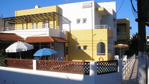A building with a yellow and white facade, a balcony with umbrellas, and a sign reading "Apartments DIMITRA". - Dimitra Apartments (Hersonissos)