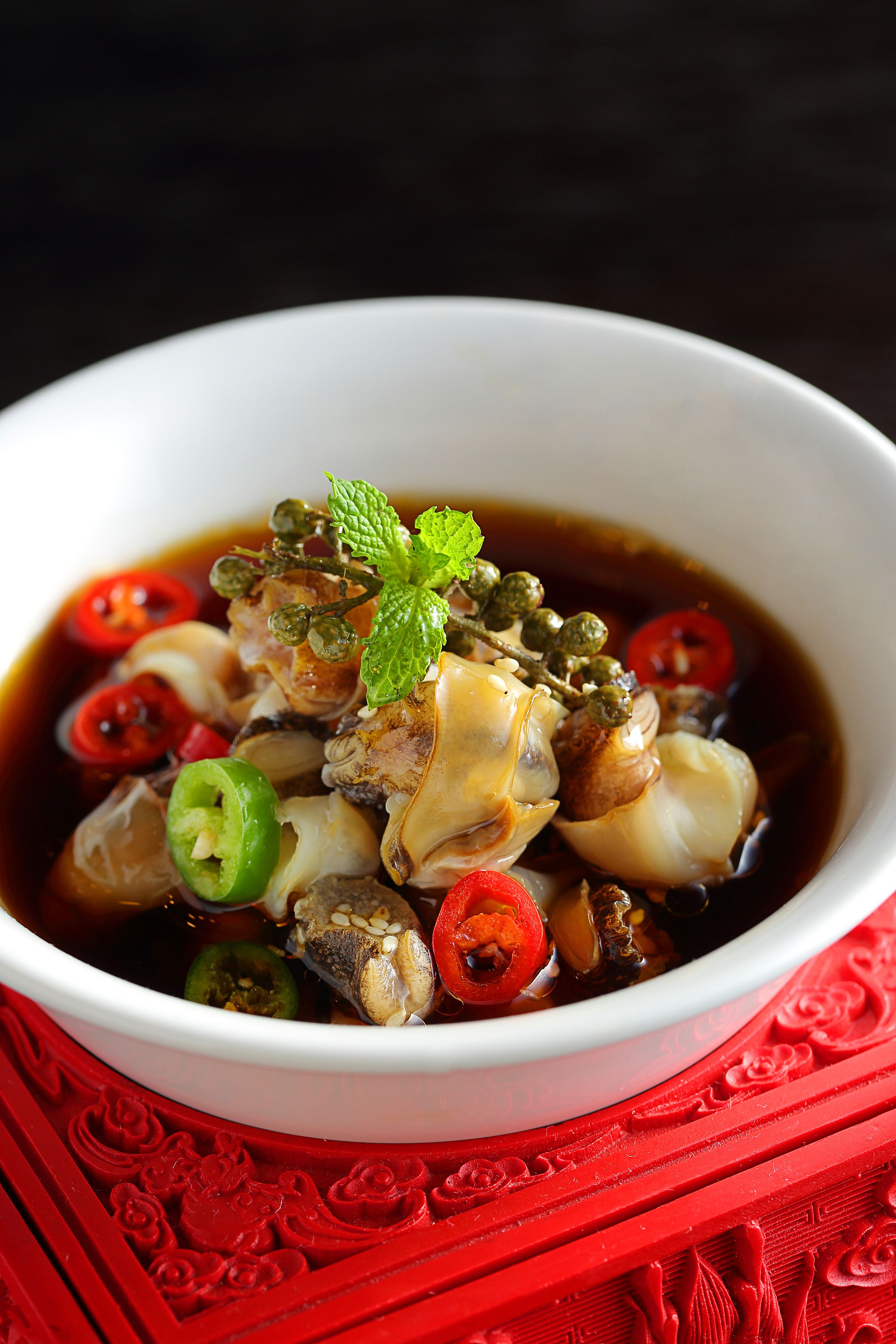 A bowl of soup with various ingredients and a mint garnish, placed on a red textured surface.