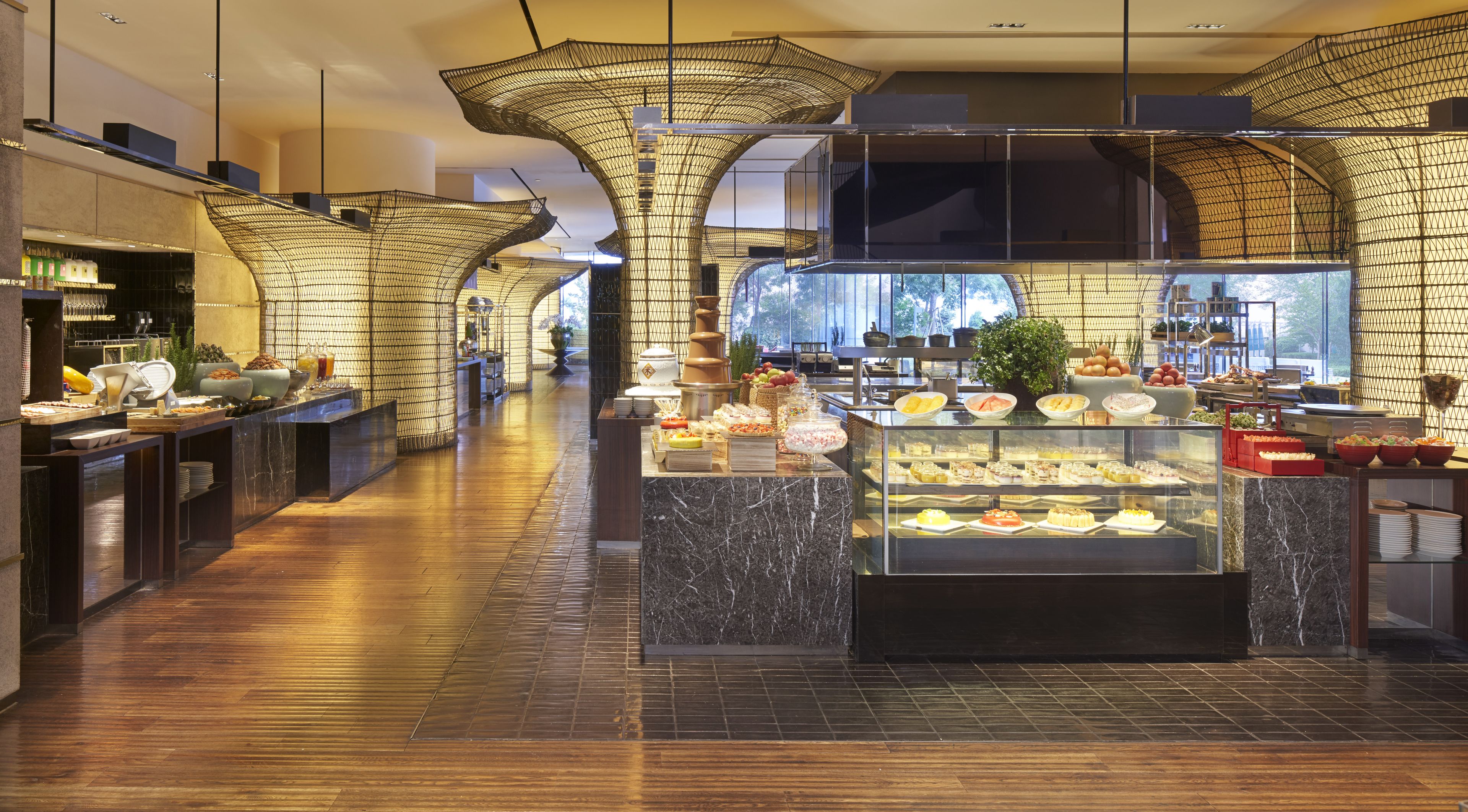 A modern hotel lobby with a marble floor, a central food display, and a large window offering a view of the outdoors.