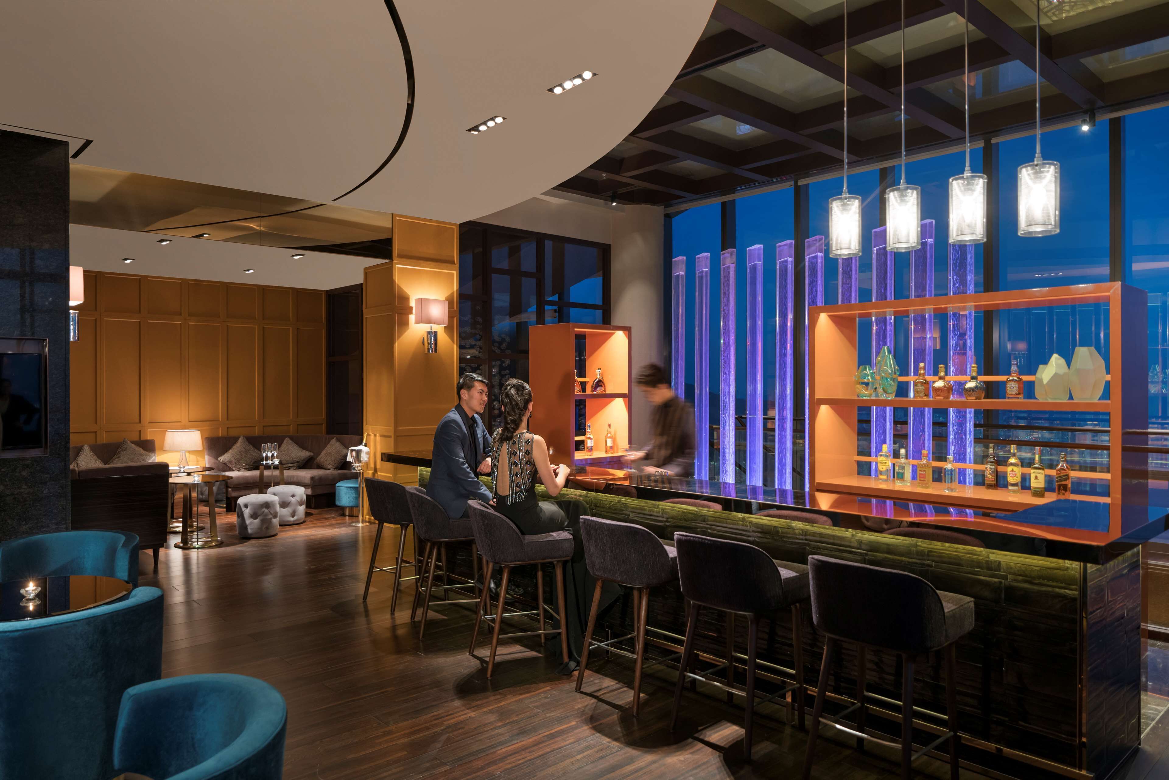 A modern bar area with a bar counter, stools, and a seating area with sofas and a coffee table.