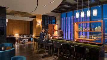 A modern bar area with a bar counter, stools, and a seating area with sofas and a coffee table.