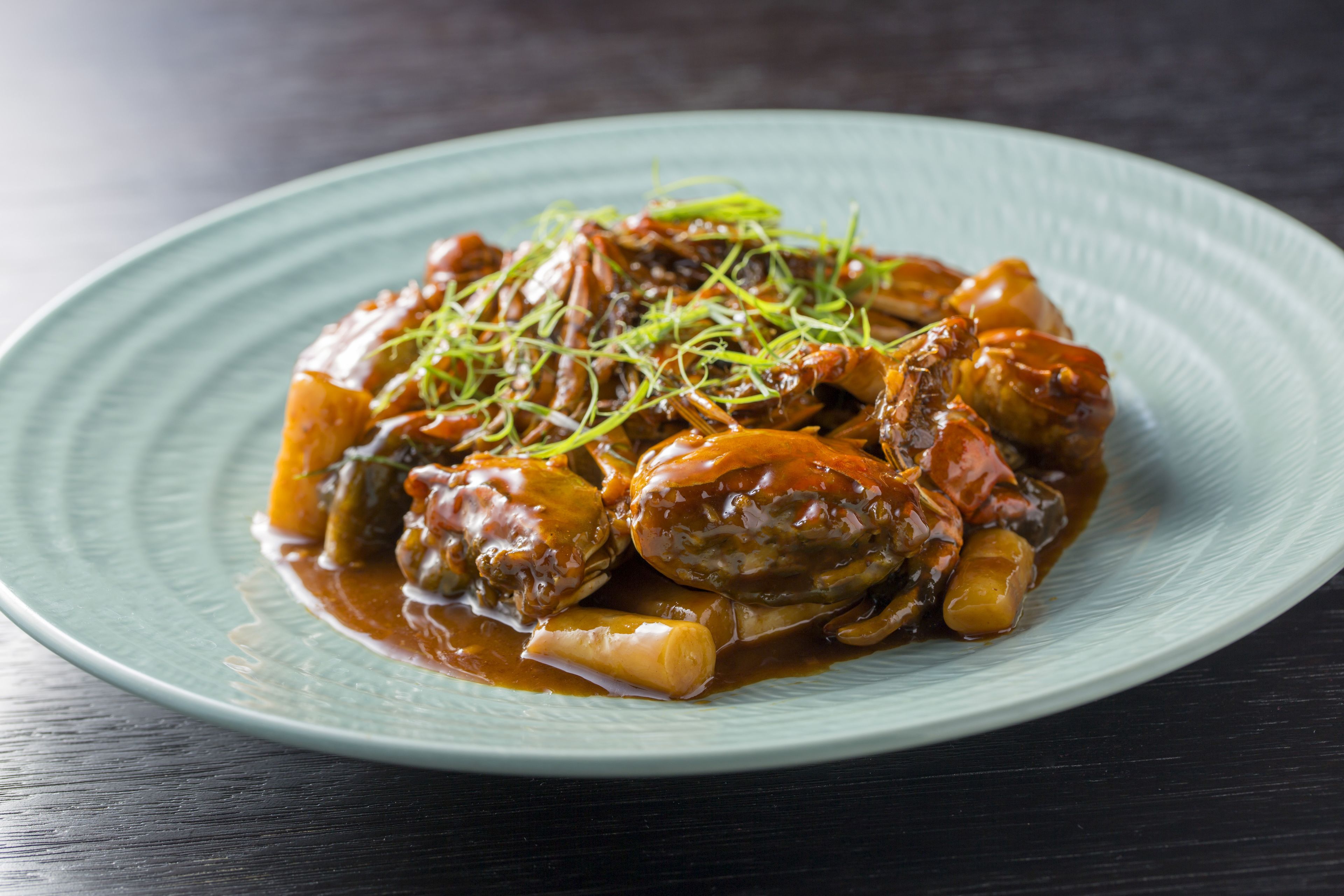 A plate of braised meat with vegetables and a garnish on a blue plate.
