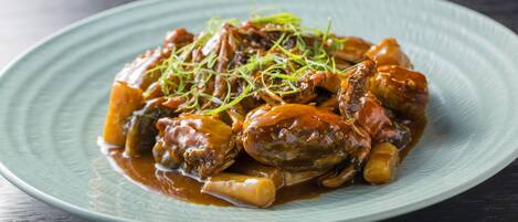 A plate of braised meat with vegetables and a garnish on a blue plate.