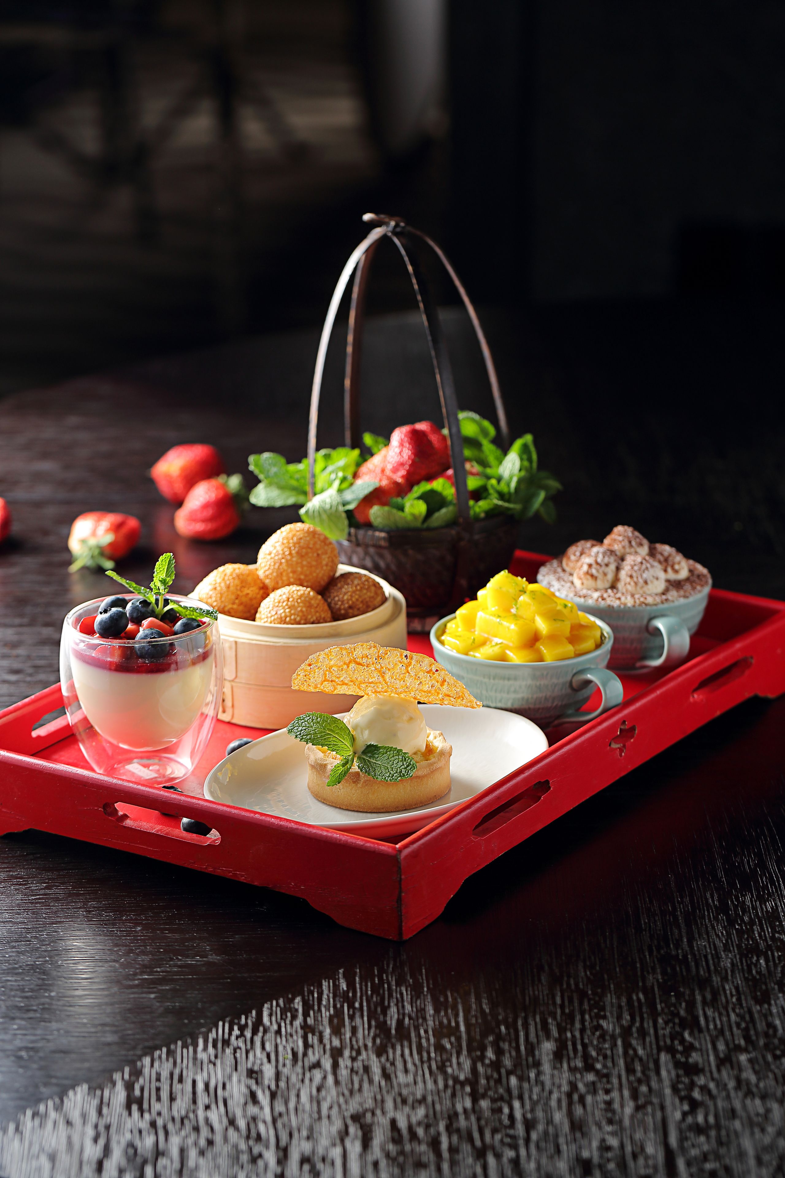 Eine Schale mit verschiedenen Desserts, darunter eine Schüssel mit Mango-Stückchen, eine Schüssel mit Schlagsahne und ein Glas Joghurt mit Beeren.