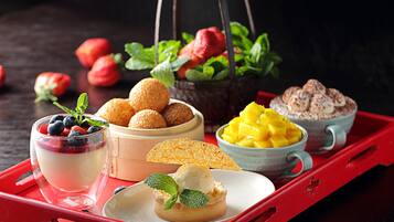 Eine Schale mit verschiedenen Desserts, darunter eine Schüssel mit Mango-Stückchen, eine Schüssel mit Schlagsahne und ein Glas Joghurt mit Beeren.