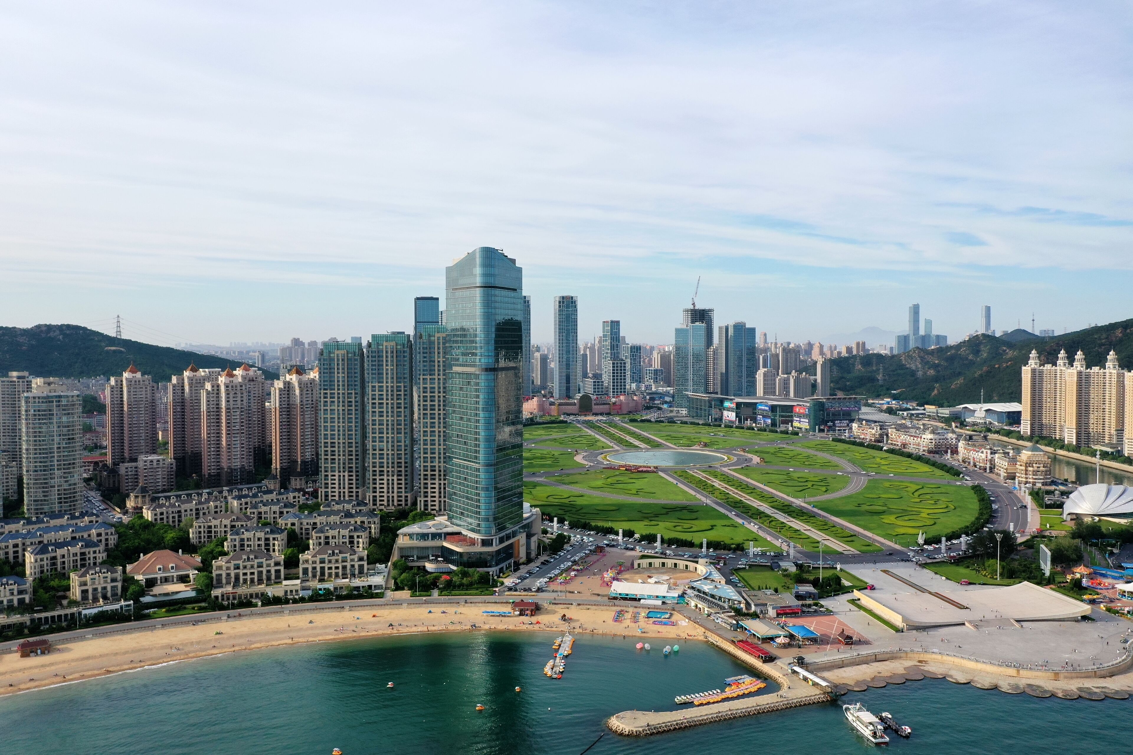 Un paisaje urbano costero con edificios altos, una playa y un puerto deportivo.
