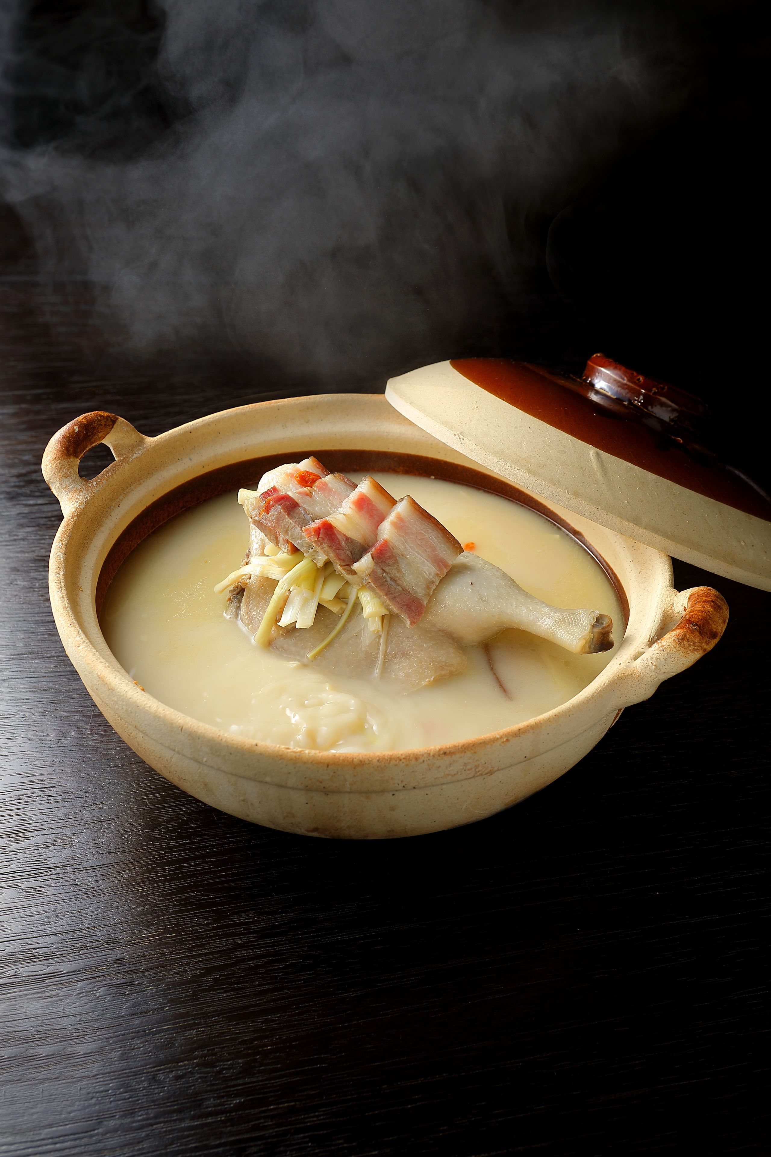 Una olla de cerámica con tapa, que contiene una sopa cremosa con carne y verduras.