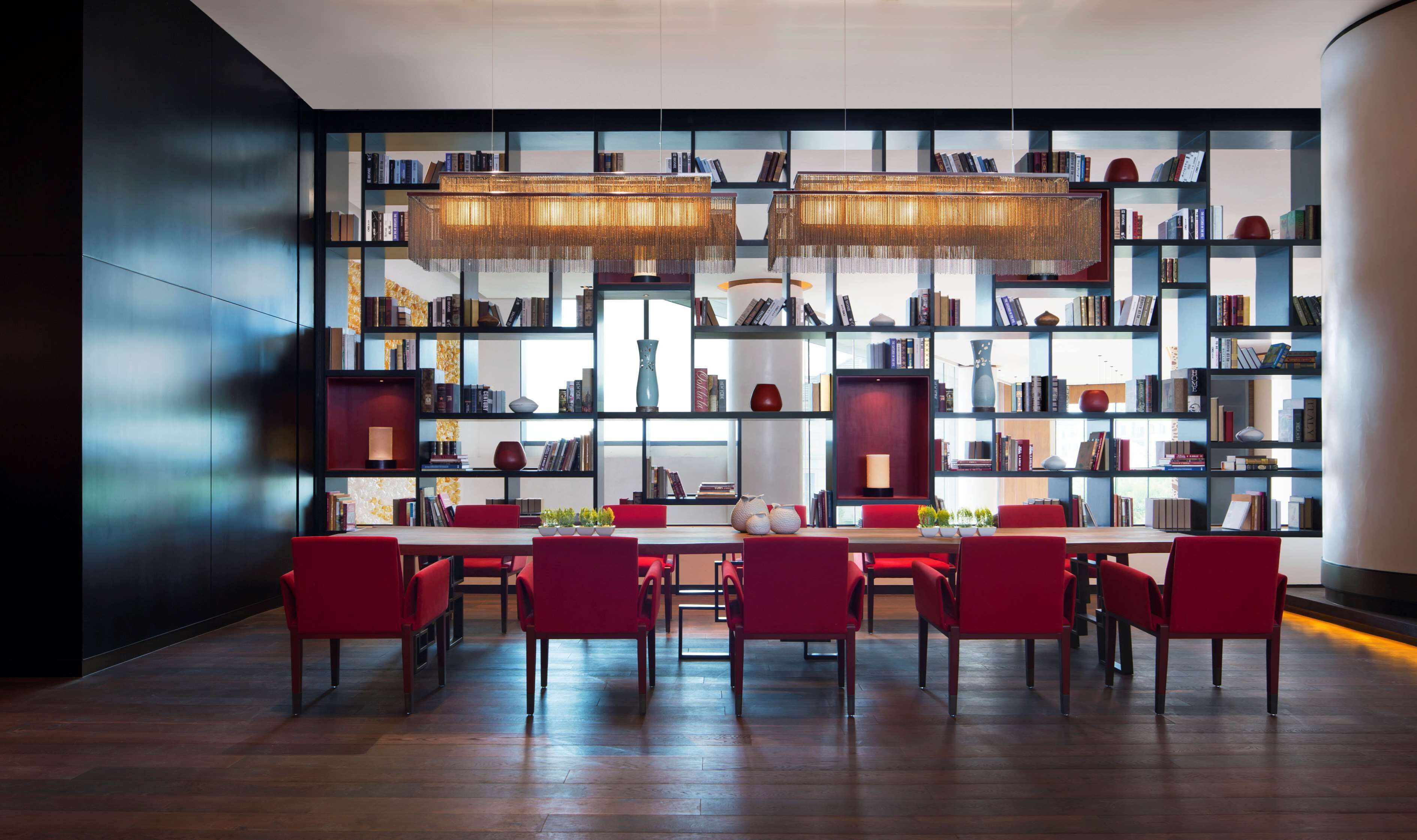 Una biblioteca moderna con una mesa de madera y sillas rojas, rodeada de estanterías llenas de libros y objetos decorativos.