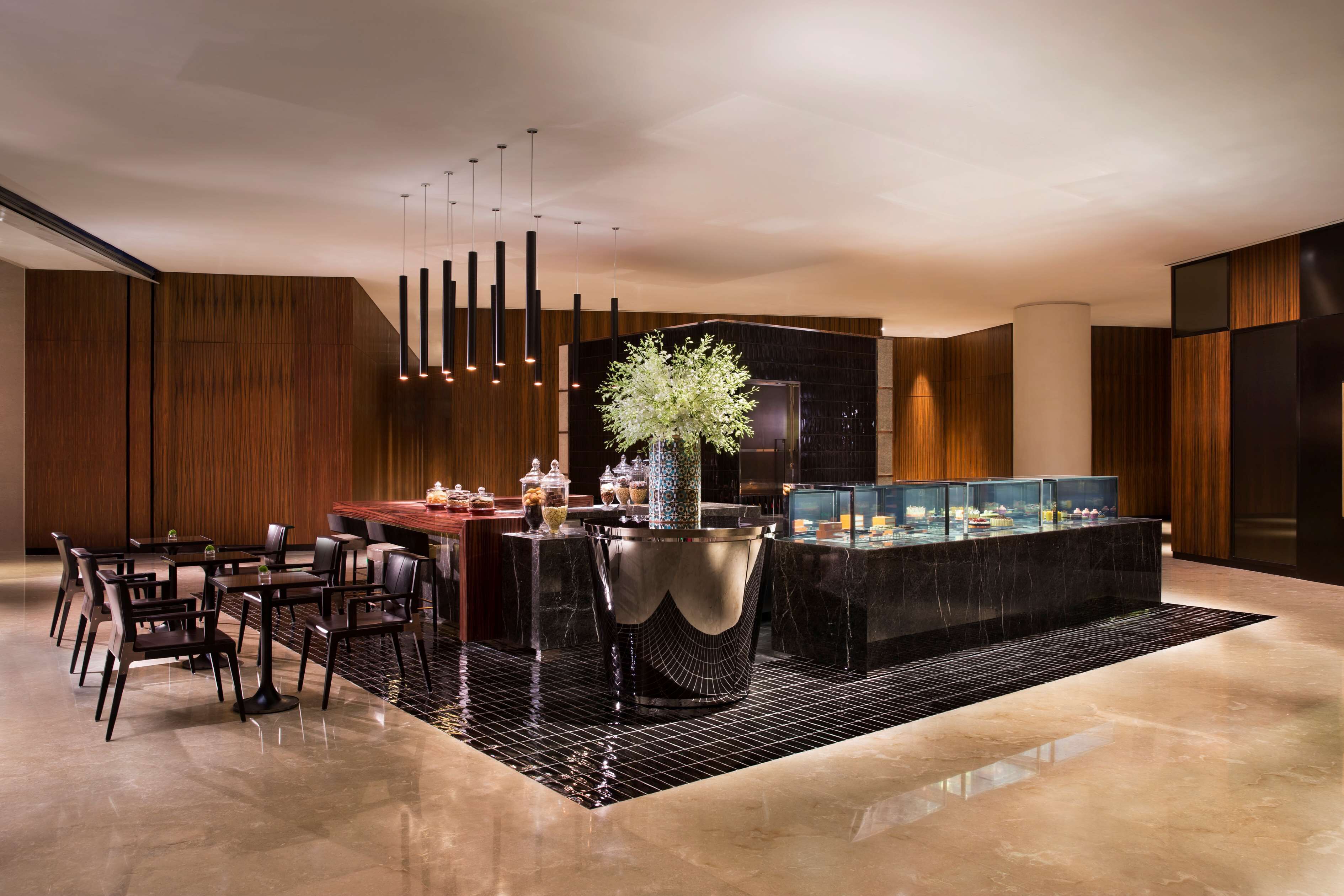 A modern hotel lobby with a central bar area, seating arrangements, and a decorative plant centerpiece.