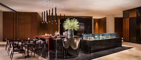 A modern hotel lobby with a central bar area, seating arrangements, and a decorative plant centerpiece.