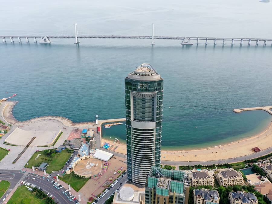 Un hotel de gran altura con diseño moderno, cerca de una playa y un puente grande.