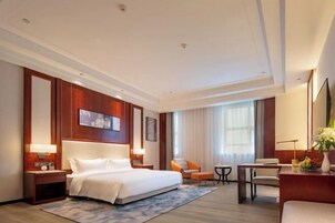 A hotel room with a large bed, a desk, a chair, and a small table.