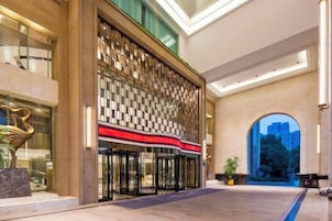 Un vestíbulo de hotel con diseño moderno, que presenta un muro con estampado, un detalle en rojo y una vista a través de un arco.