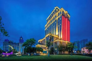 A multi-story hotel with a prominent red facade, surrounded by a well-maintained lawn and other buildings. - Nanxi Juyang Hotel (Yibin)