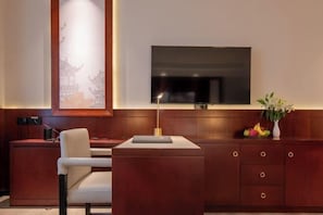 Una habitación moderna con televisión de pantalla plana montada en la pared, un mueble de madera con cajones, un escritorio y una silla.