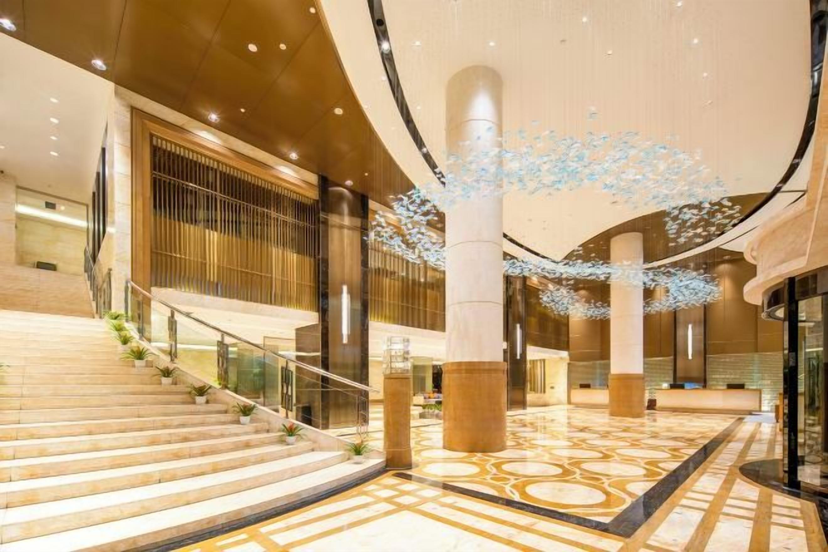 Eine geräumige Lobby mit einer imposanten Treppe, großen Säulen und einer dekorativen Lichtinstallation.