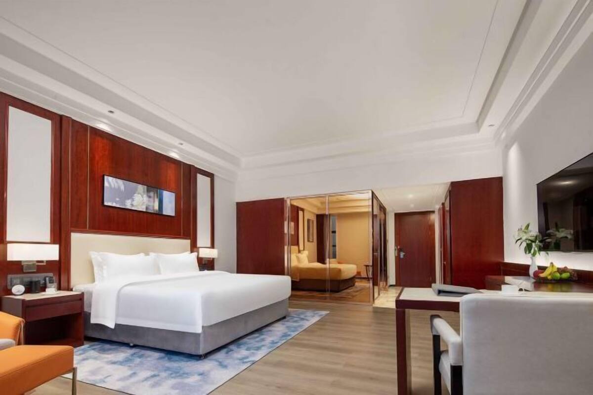 Ein Hotelzimmer mit einem großen Bett, einem Schreibtisch und einem Stuhl. An der Wand hängt ein Spiegel und auf dem Schreibtisch steht ein Fernseher.