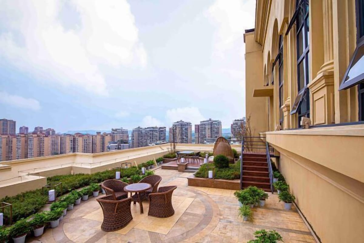 Una terraza en la azotea con mobiliario exterior, plantas en macetas y vistas de edificios altos circundantes.