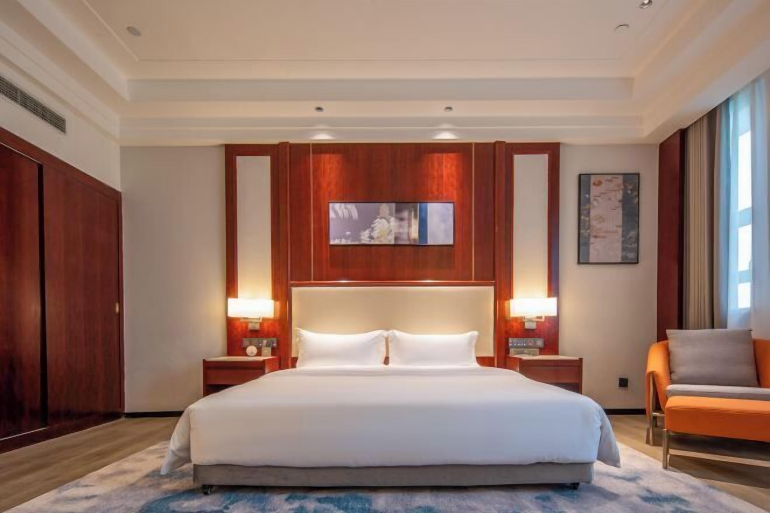 A hotel room with a large bed, two bedside tables with lamps, a wooden wardrobe, and a painting on the wall.