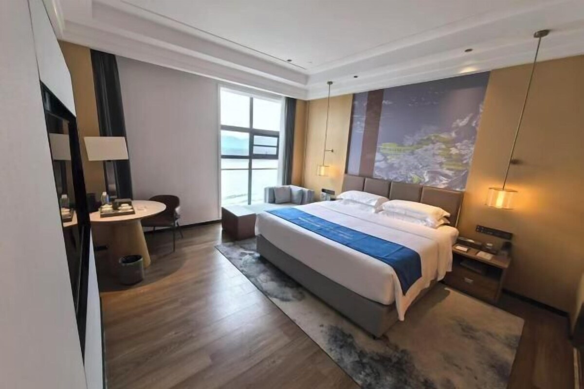 A modern hotel room with a large bed, a desk, and a window with a view.