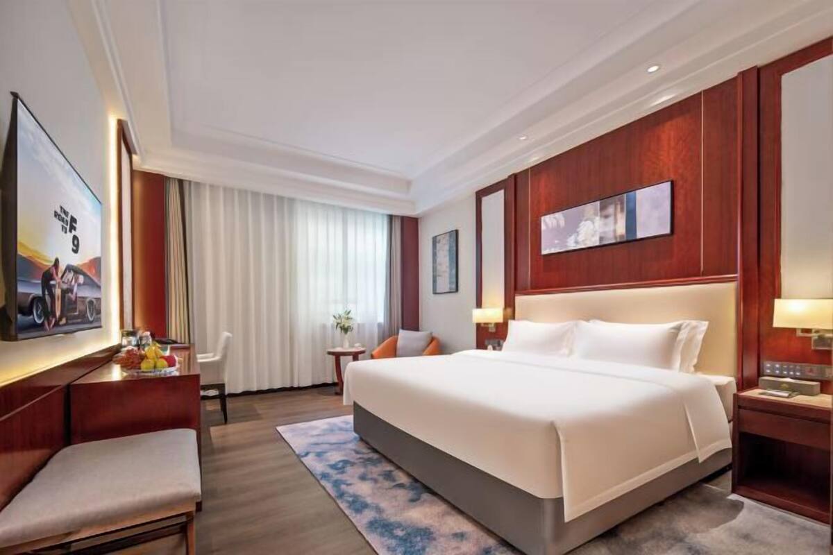 Ein Hotelzimmer mit einem großen Bett, einem Schreibtisch mit Stuhl, einem Fernseher und einem Bild an der Wand.