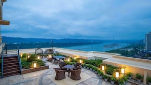 A rooftop terrace with outdoor seating, potted plants, and a view of a bridge and cityscape. - Nanxi Juyang Hotel (Yibin)