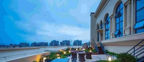 A rooftop terrace with outdoor seating, a staircase, and a view of the cityscape.