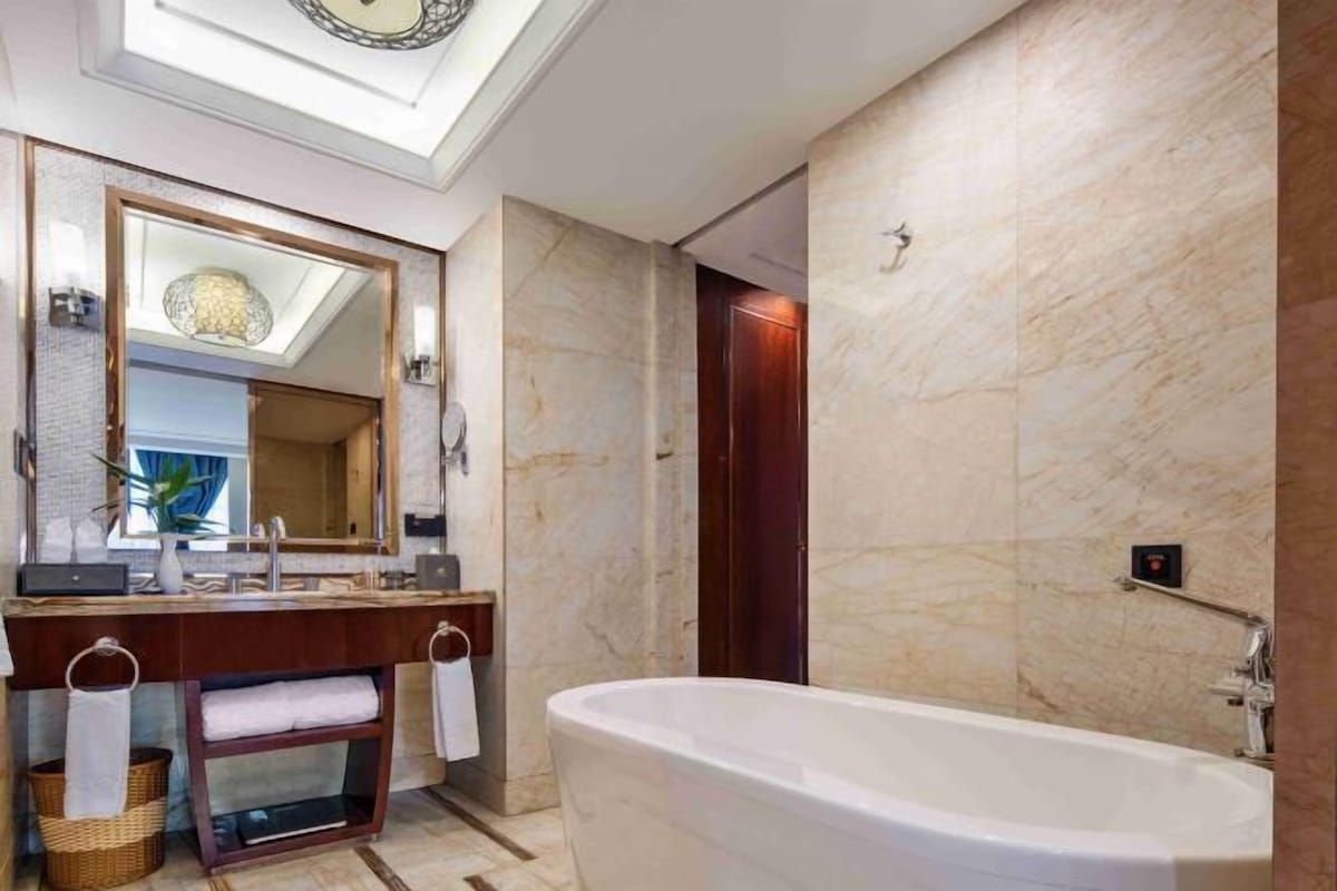 Un baño moderno con una bañera independiente, un espejo grande y un tocador con lavamanos y perchero para toallas.