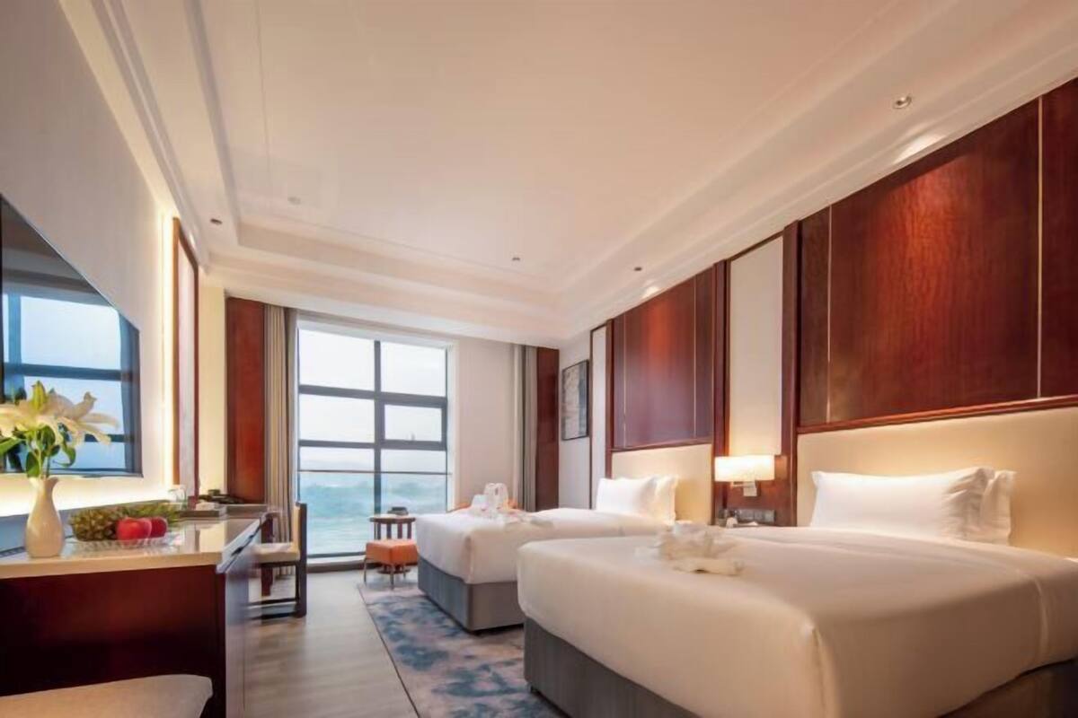 Ein Hotelzimmer mit zwei Betten, einem Schreibtisch, einem Stuhl, einem Fenster mit Aussicht und einem großen Spiegel.