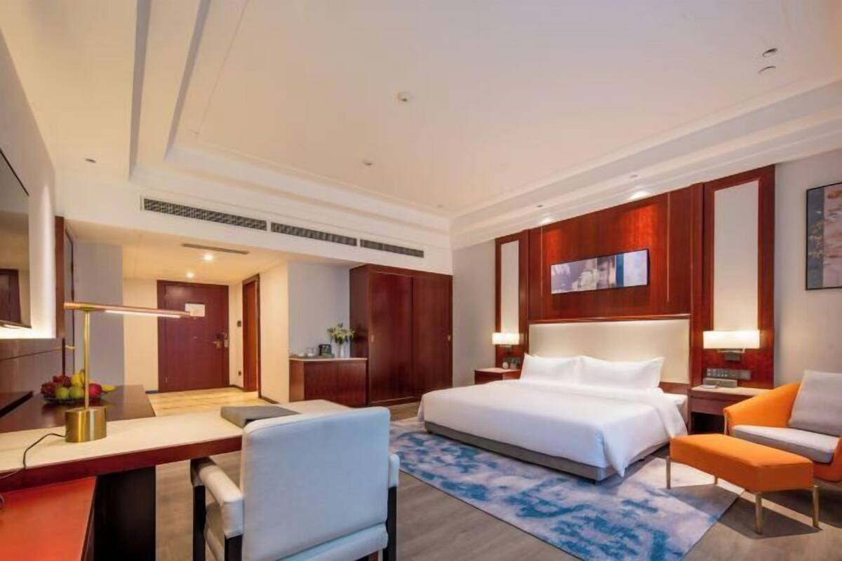 Ein Hotelzimmer mit einem großen Bett, einem Schreibtisch, einem Sessel, einem Fernseher und einem Holzschrank.