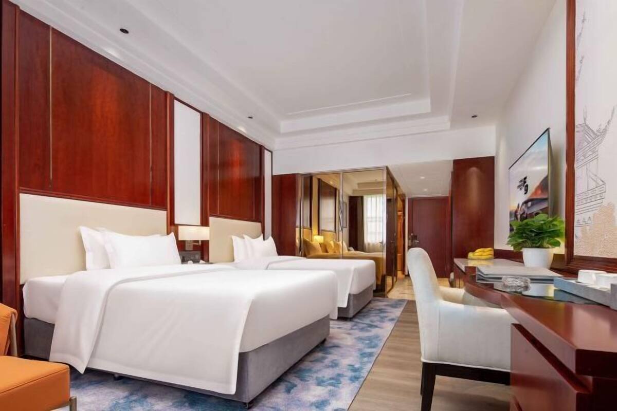 Ein Hotelzimmer mit zwei Betten, einem Schreibtisch, einem Stuhl, einem Spiegel und einer Topfpflanze.