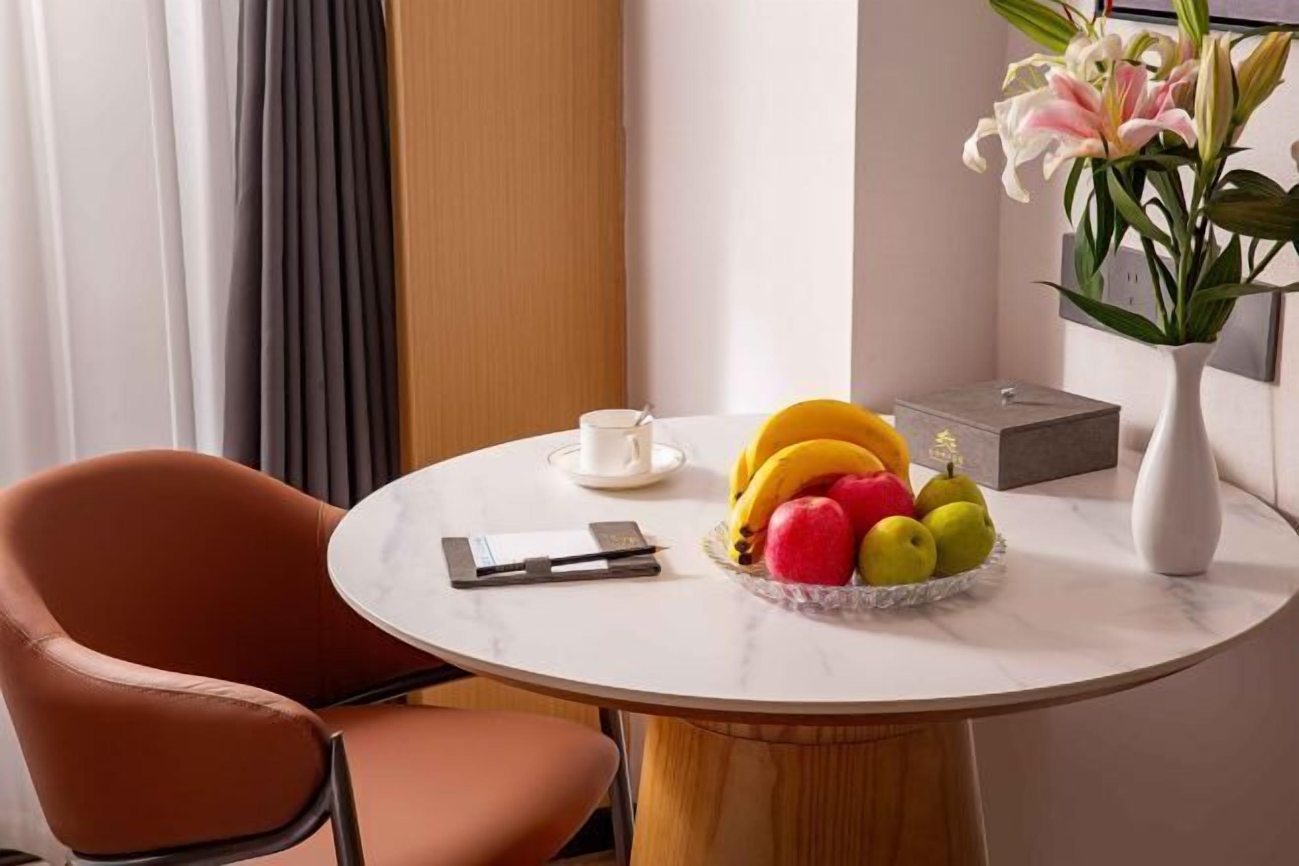 A round marble table with a fruit bowl, a white cup, and a vase with flowers.