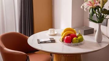 A round marble table with a fruit bowl, a white cup, and a vase with flowers.