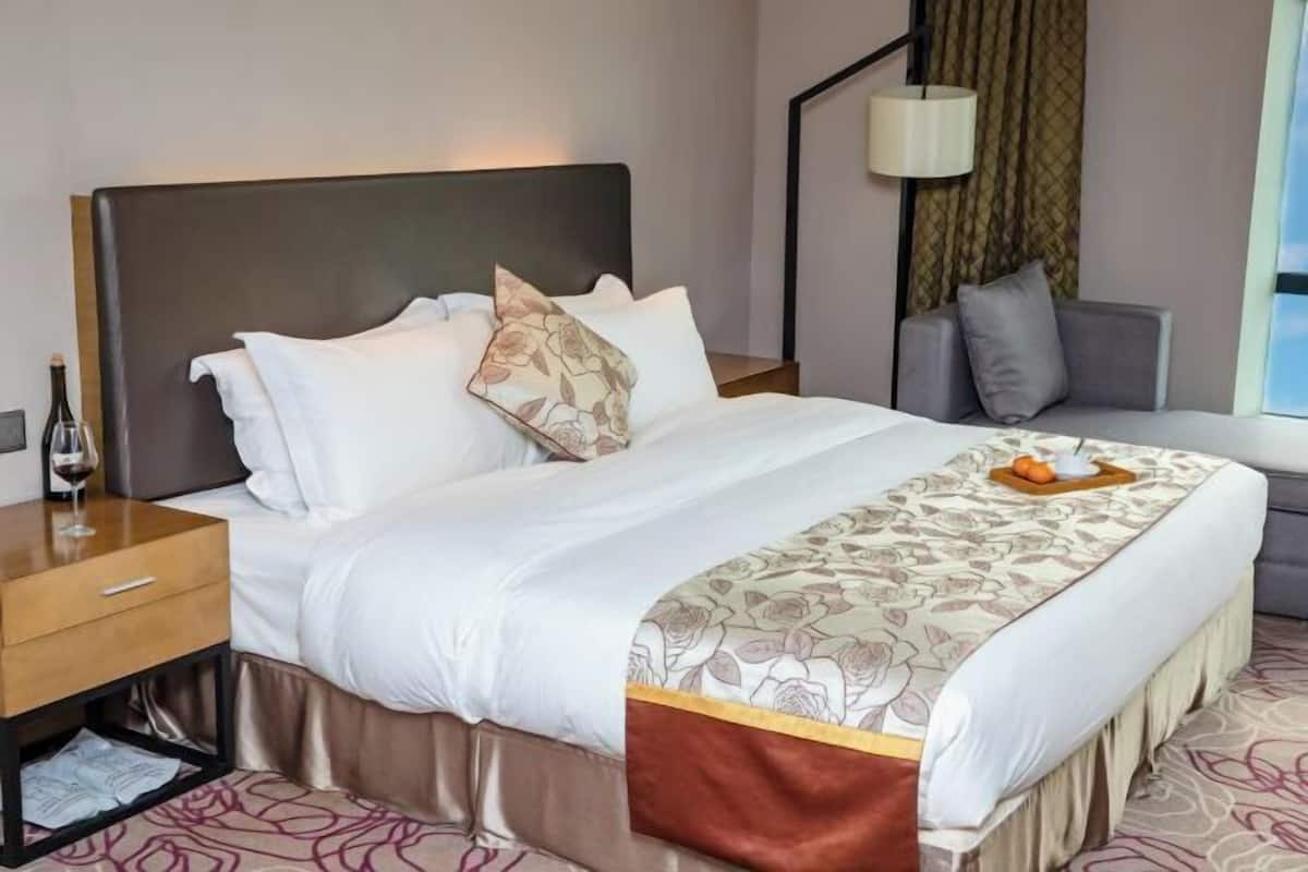 A hotel room with a bed, bedside table, lamp, and a view of the outdoors.