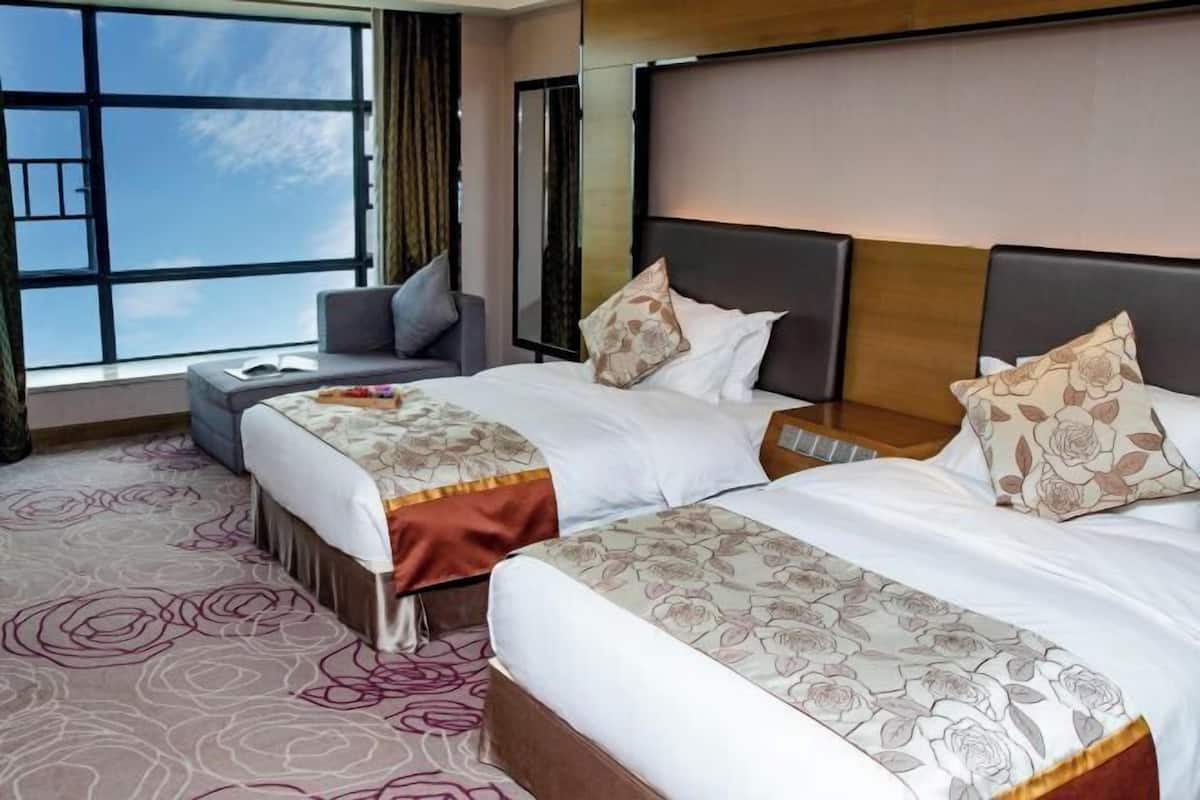 A hotel room with two beds, a sofa, a large window, and a patterned carpet.