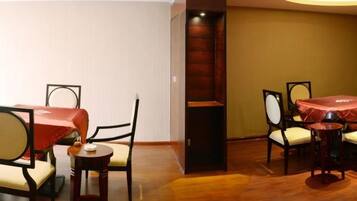 A hotel room with a bed, a small table, two chairs, a dining table with a red tablecloth, and a wooden partition.