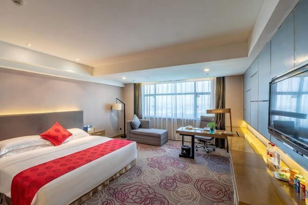 A hotel room with a bed, a desk, a chair, a TV, and a large window.
