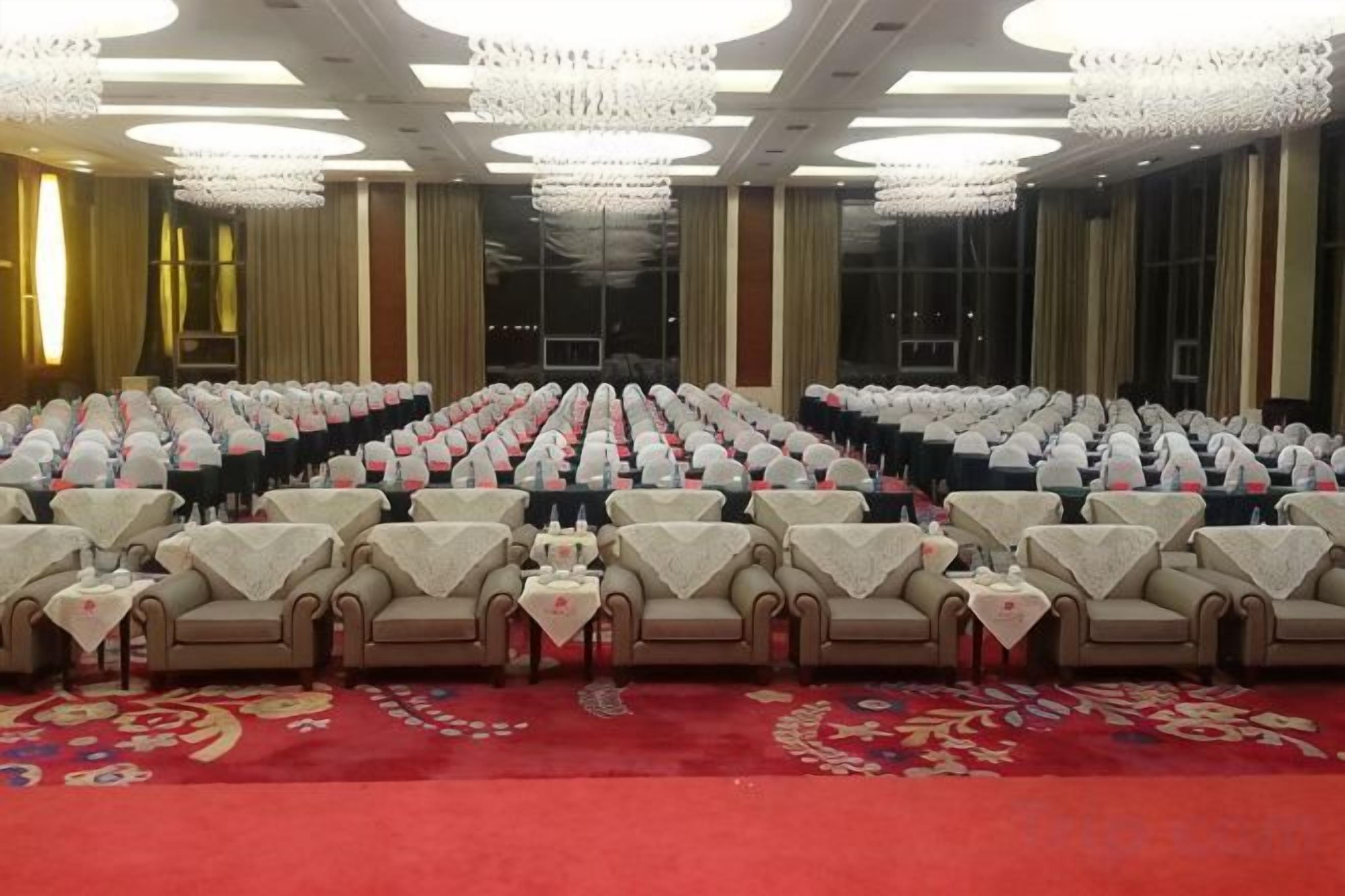 Un salón de conferencias con filas de sillas y mesas, ventanas amplias y candelabros.