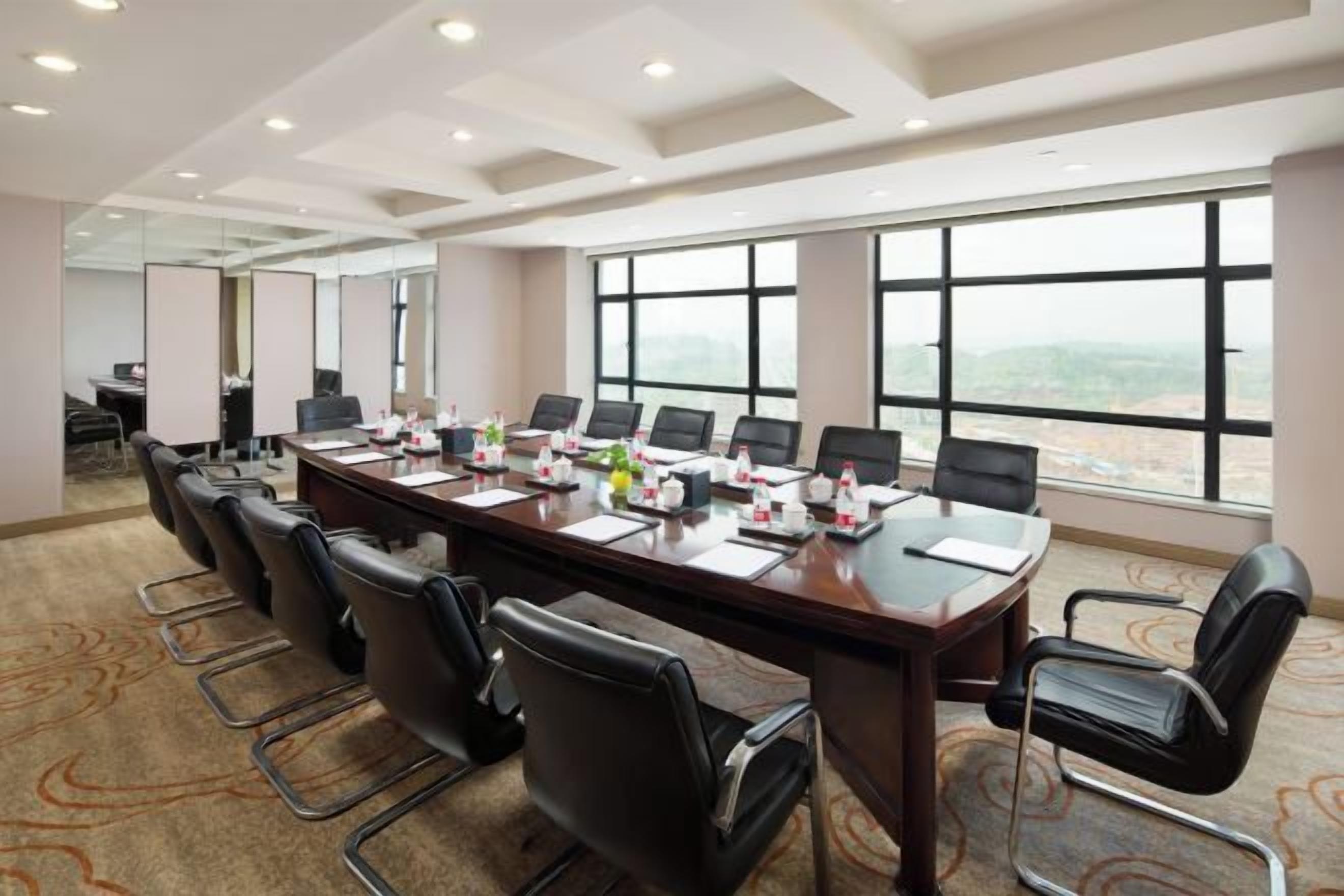 A conference room with a long table, multiple chairs, and a view through large windows.