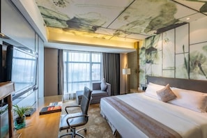 A hotel room with a bed, desk, chair, large windows, and artwork on the walls. - Huatian Hotel (Shaoyang)
