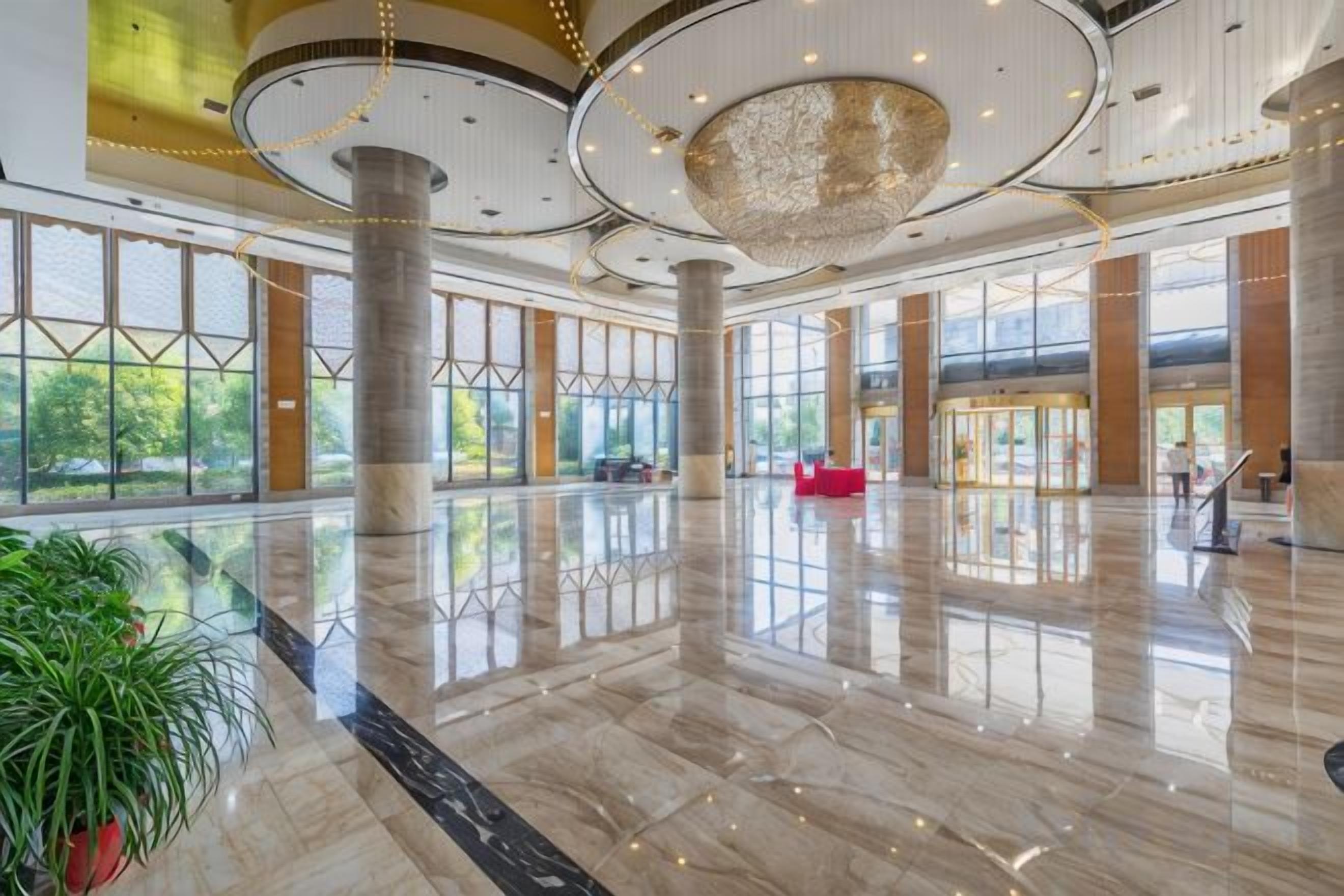 A spacious lobby with a polished marble floor, large windows, and a central chandelier.