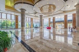 Un vestíbulo amplio con piso de mármol pulido, ventanas grandes y un candelabro central.