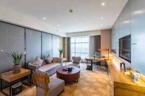 A modern hotel room with a sofa, armchair, coffee table, TV, and a large window. - Huatian Hotel (Shaoyang)