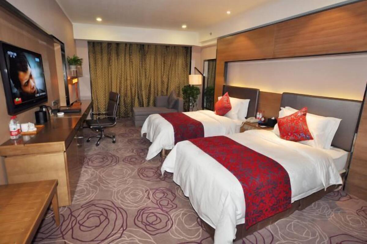 A hotel room with two beds, a desk, a television, and a large window with curtains.