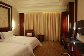 Een hotelkamer met een bed, een bureau, een stoel, een televisie en een gordijn.