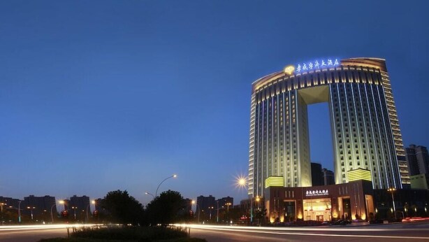 A tall, modern hotel with a distinctive arch entrance, surrounded by other buildings and a busy street at dusk. - Yuji Royal Grand Hotel (Xiaogan)