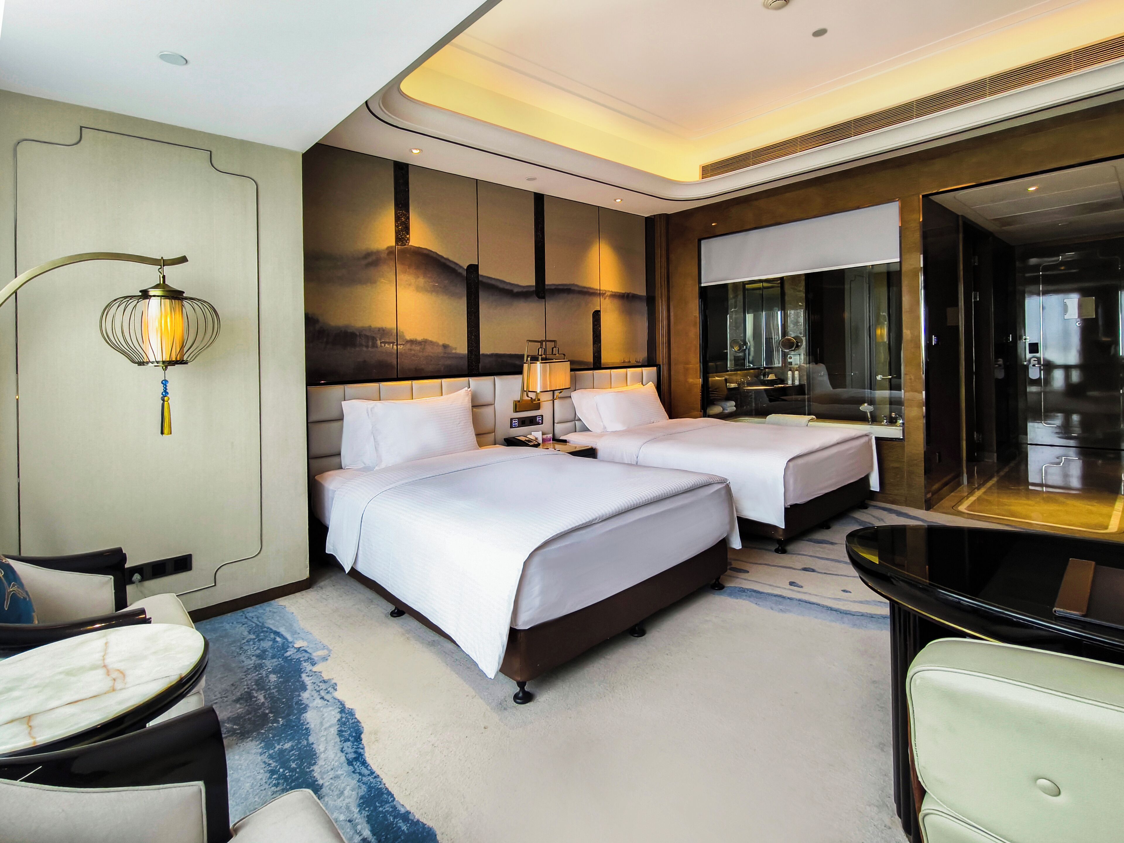 Ein Hotelzimmer mit zwei Betten, einer Sitzecke mit Tisch und Stühlen, einem großen Spiegel und einem dekorativen Wandbild.