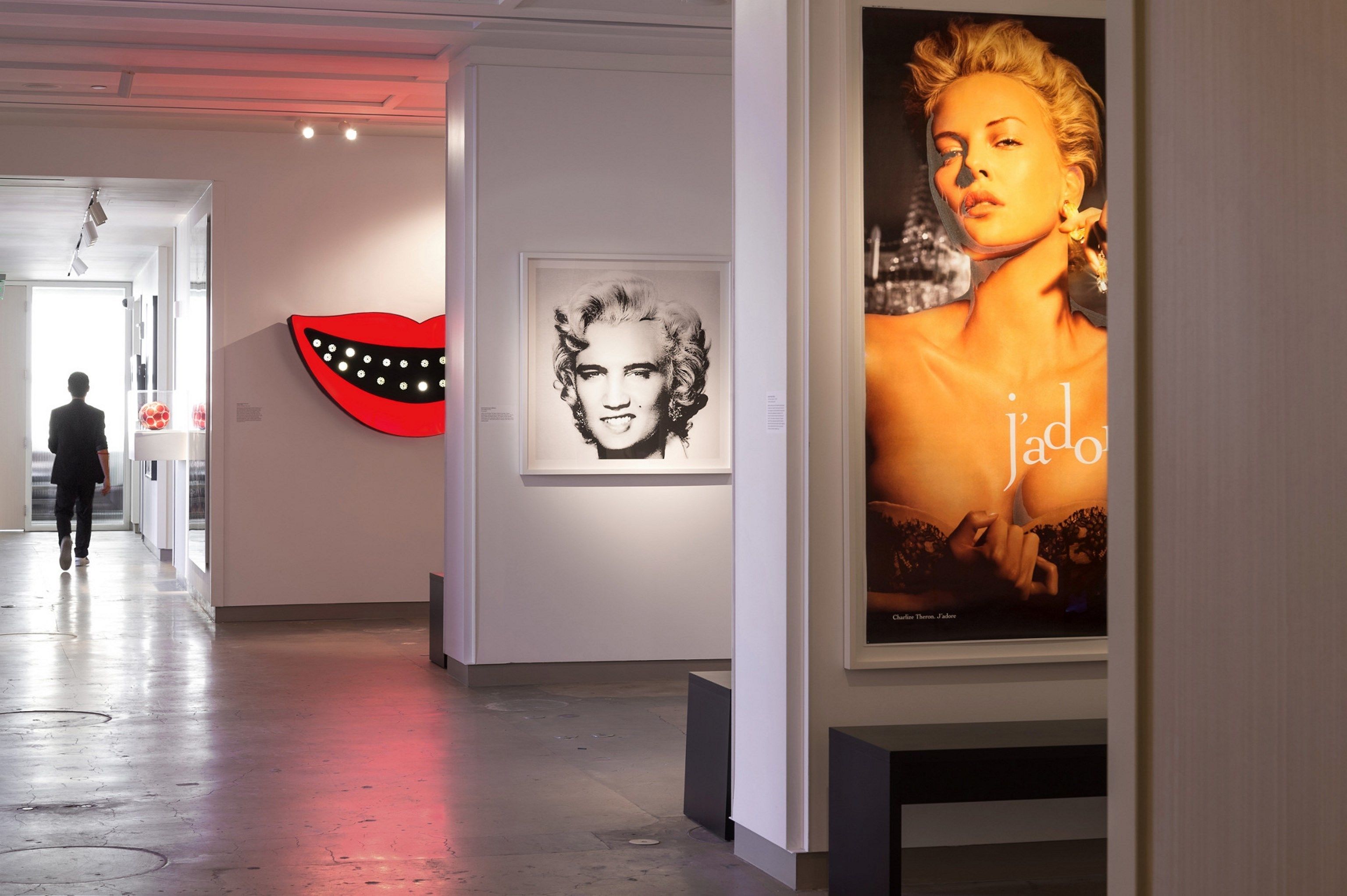 An art gallery with framed artworks on the walls, a red lips sculpture, and a poster.
