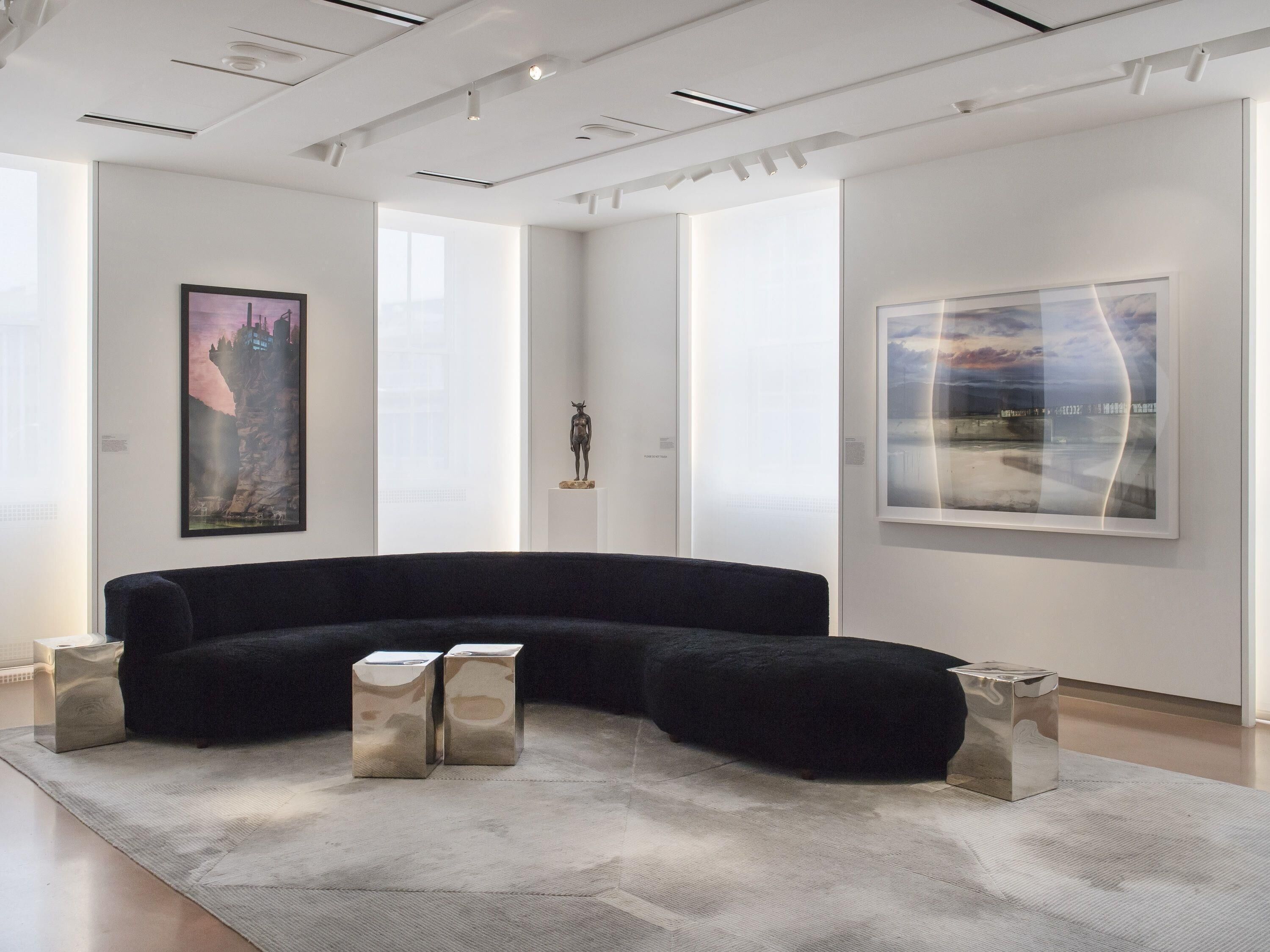 A modern art gallery with abstract paintings, a black sofa, and minimalist decor.